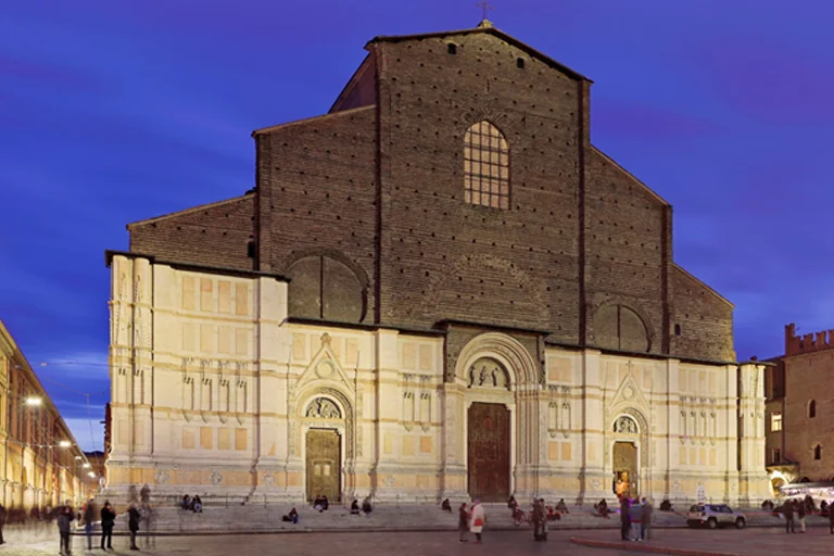 Front view of Basilica of San Petronio at dusk with large brick facade and illuminated marble entrance in Bologna Italy