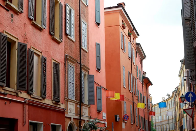 Narrow Bologna street lined with pastel colored buildings, shutters and traditional Italian architecture
