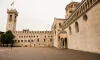 Wide stone plaza with historic cathedral building, arched colonnades and medieval clock tower in a quiet Italian city square